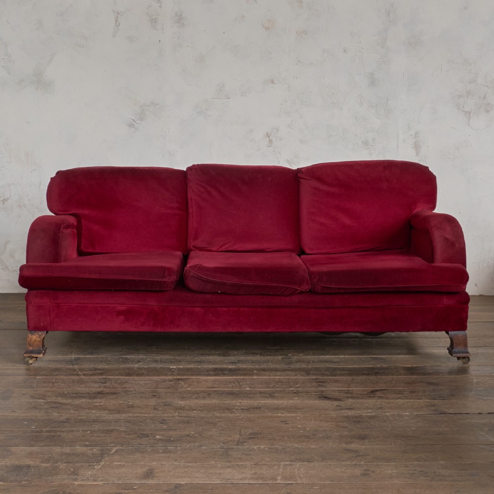 A side profile of a deep crimson velvet antique sofa featuring scroll arms and dark wood castors. View VI