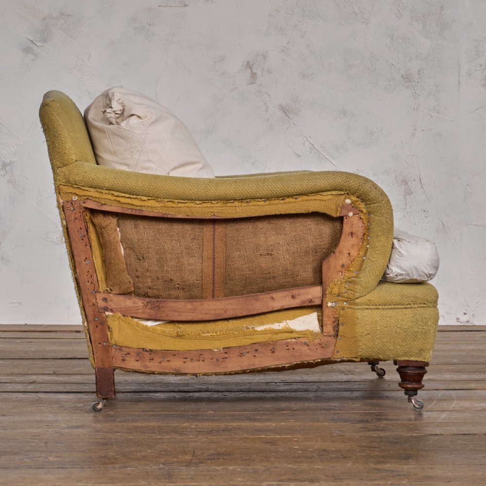 An antique deep-seated armchair with exposed hessian framing, olive green fabric, and turned wooden legs with castors. View VI