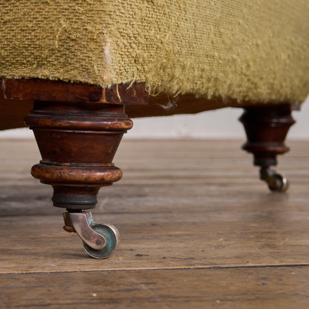 An antique deep-seated armchair with exposed hessian framing, olive green fabric, and turned wooden legs with castors. View VII