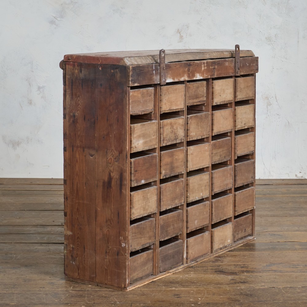 An antique multi-drawer wooden cabinet featuring a red painted finish, numerous small drawers with metal cup handles, and decorative wooden spool moulding along the top edge. View V