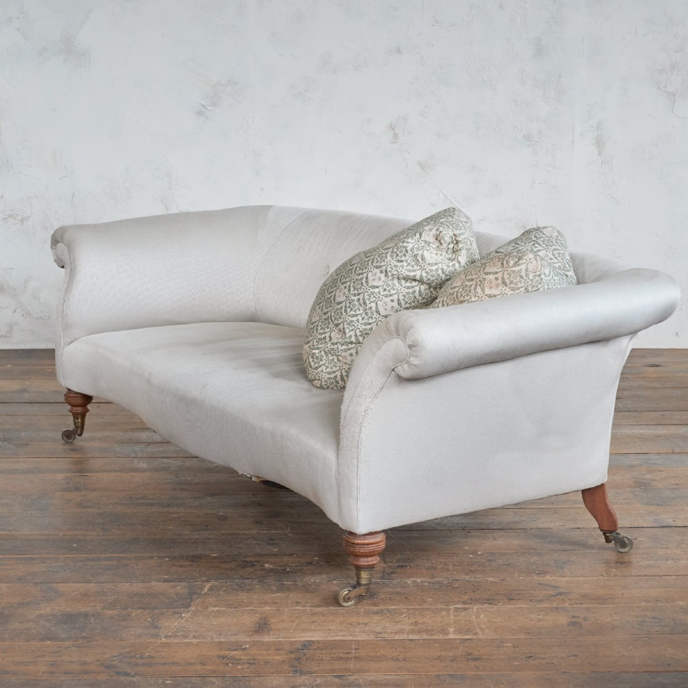 An off-white upholstered Victorian sofa with a curved back, rolled arms, and turned wooden legs fitted with brass castors.