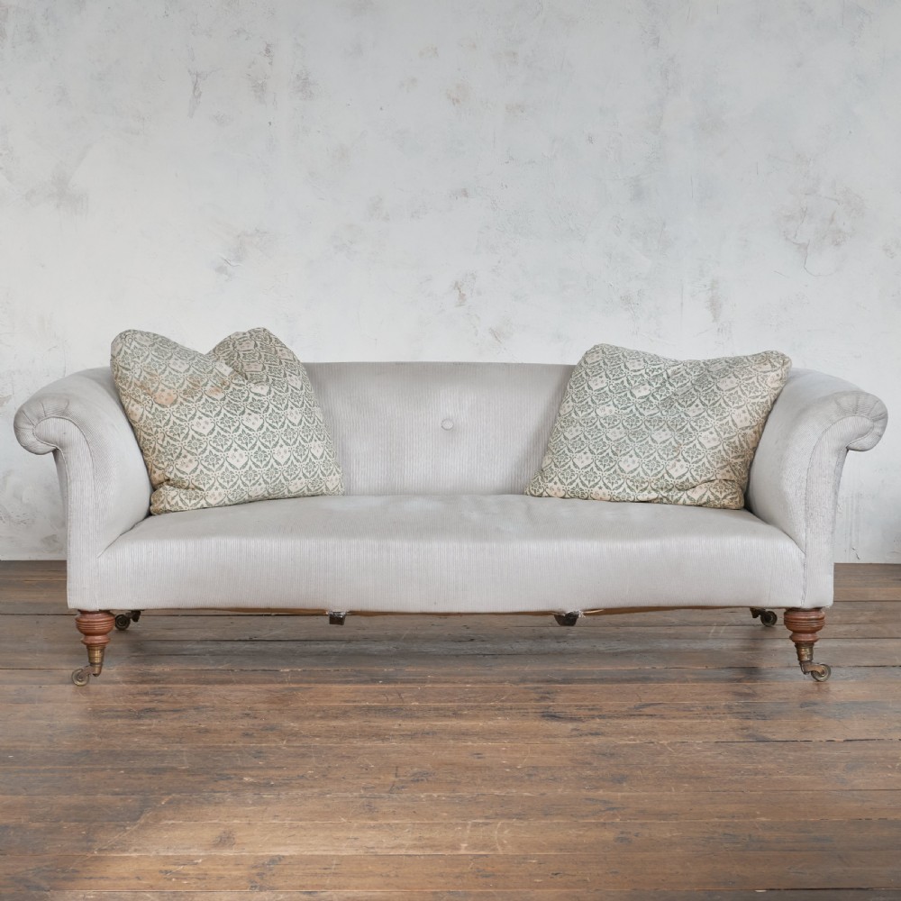 An off-white upholstered Victorian sofa with a curved back, rolled arms, and turned wooden legs fitted with brass castors. View II