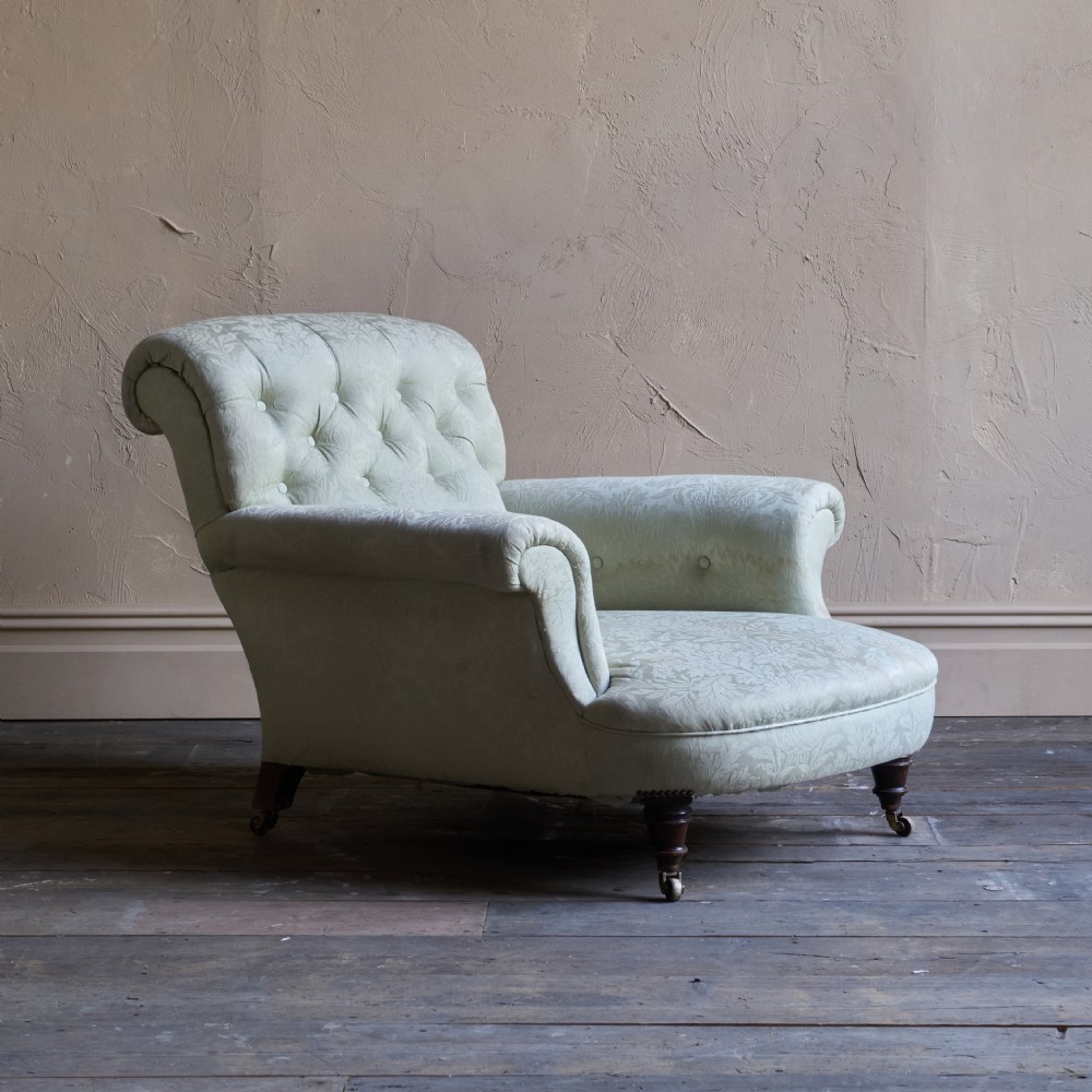 An antique sage green damask upholstered armchair with rolled arms, button tufting, and turned wooden legs with brass castors.