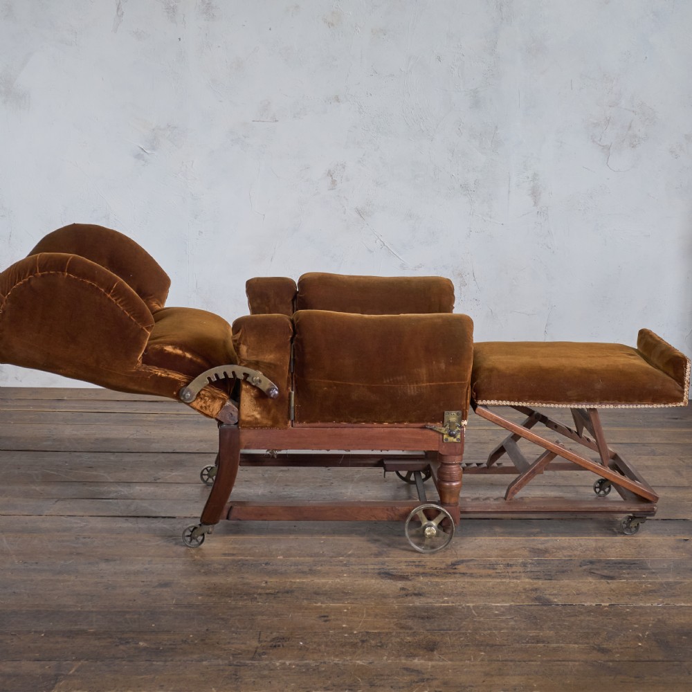 An antique Victorian mechanical reclining armchair upholstered in brown velvet with a button-tufted backrest, padded armrests, and an extendable footrest on brass castors. View II