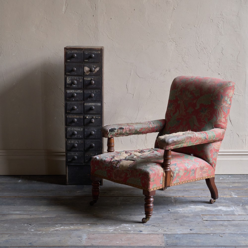 A vintage open armchair featuring a wooden frame, turned front legs on castors, and worn patterned pink upholstery. View XII