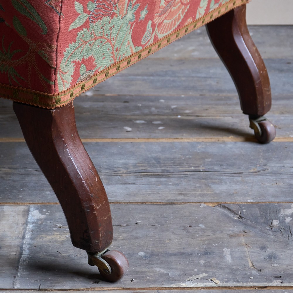A vintage open armchair featuring a wooden frame, turned front legs on castors, and worn patterned pink upholstery. View IV