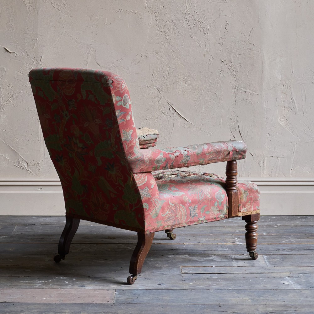 A vintage open armchair featuring a wooden frame, turned front legs on castors, and worn patterned pink upholstery. View IX