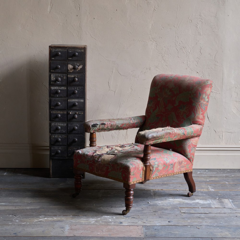 A vintage open armchair featuring a wooden frame, turned front legs on castors, and worn patterned pink upholstery. View XIII