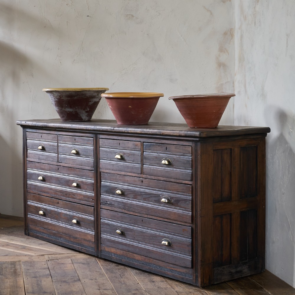 An antique wooden haberdashery counter featuring multiple rows of shallow drawers with brass cup handles.