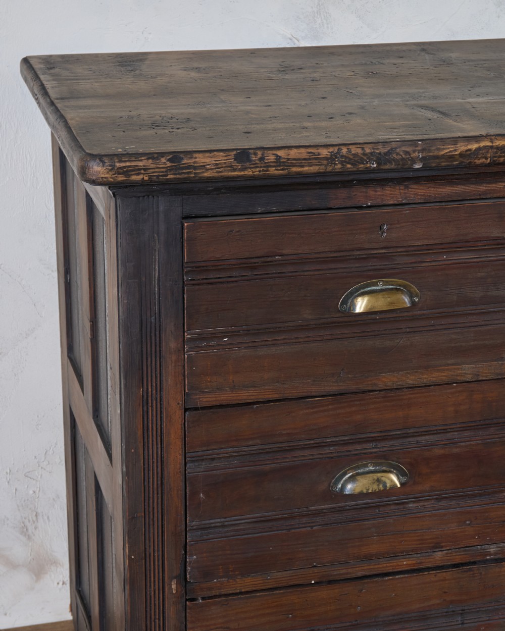 An antique wooden haberdashery counter featuring multiple rows of shallow drawers with brass cup handles. View III