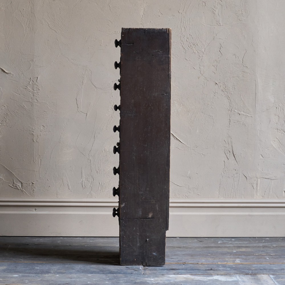 A tall and narrow antique dark wood ironmongers chest featuring sixteen small drawers with turned knobs and hand-painted white labels. View IV