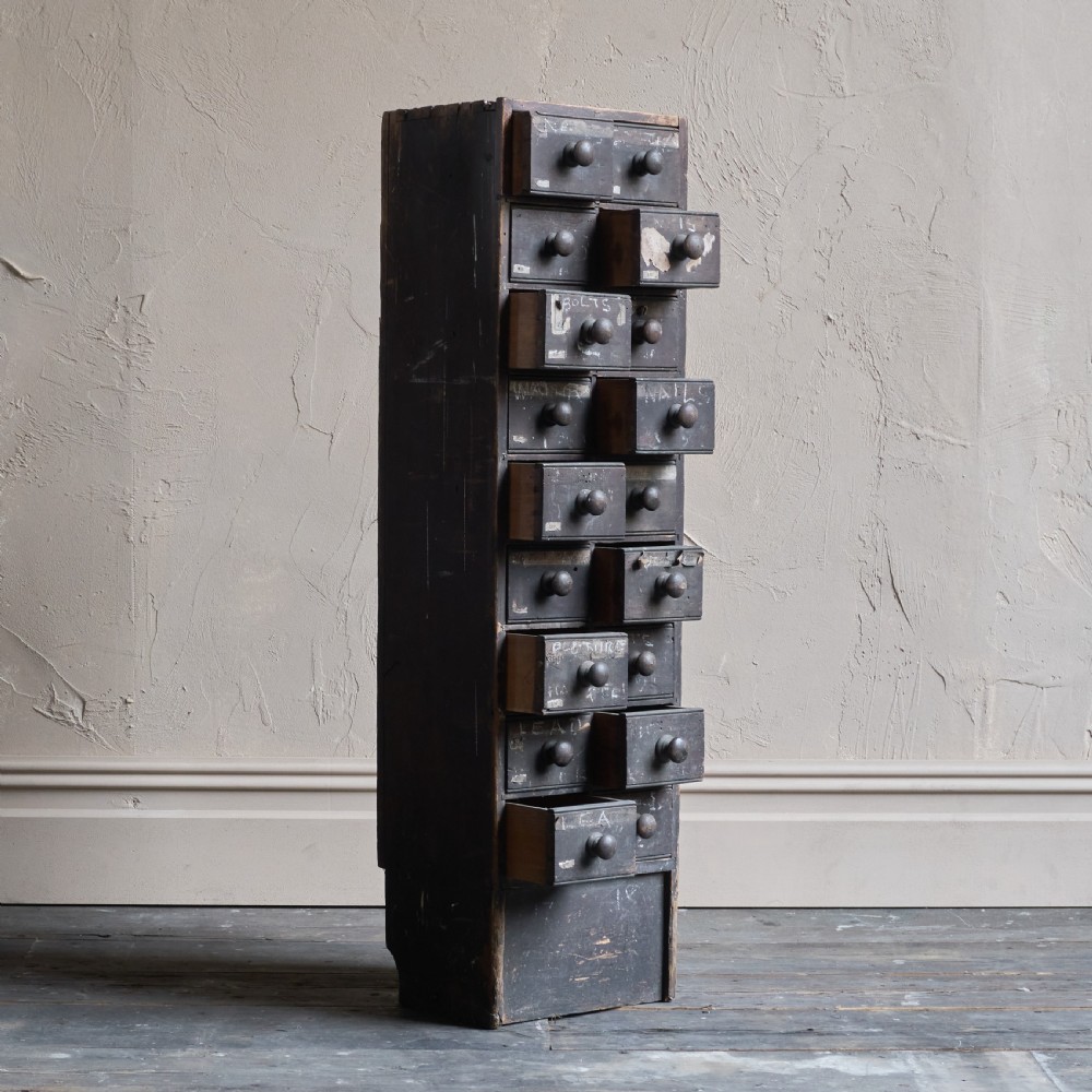 A tall and narrow antique dark wood ironmongers chest featuring sixteen small drawers with turned knobs and hand-painted white labels. View VI