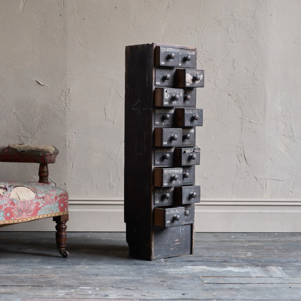 A tall and narrow antique dark wood ironmongers chest featuring sixteen small drawers with turned knobs and hand-painted white labels. View VII