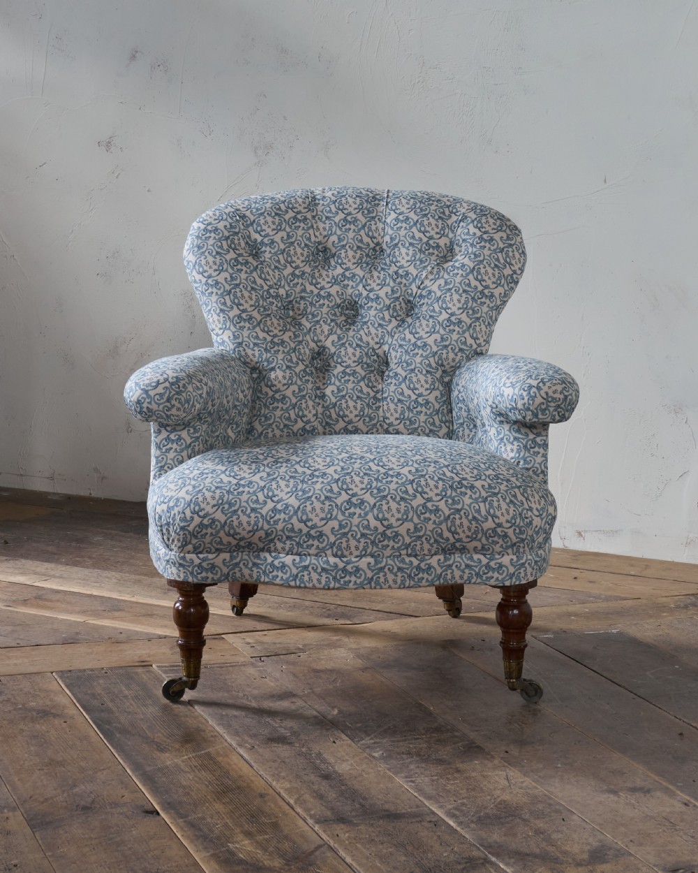 A Victorian Howard style armchair upholstered in blue and white scroll printed fabric with deep buttoning and turned mahogany legs on brass castors. View II