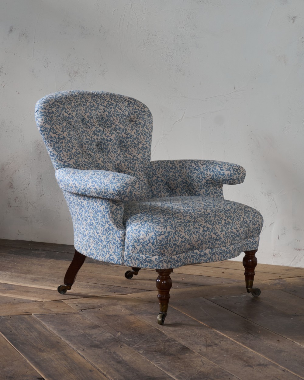 A Victorian Howard style armchair upholstered in blue and white scroll printed fabric with deep buttoning and turned mahogany legs on brass castors. View III