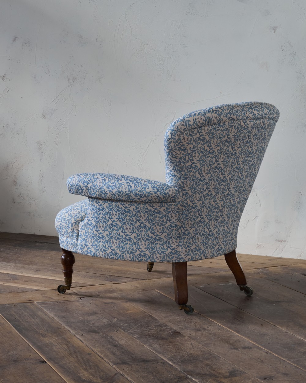 A Victorian Howard style armchair upholstered in blue and white scroll printed fabric with deep buttoning and turned mahogany legs on brass castors. View IV