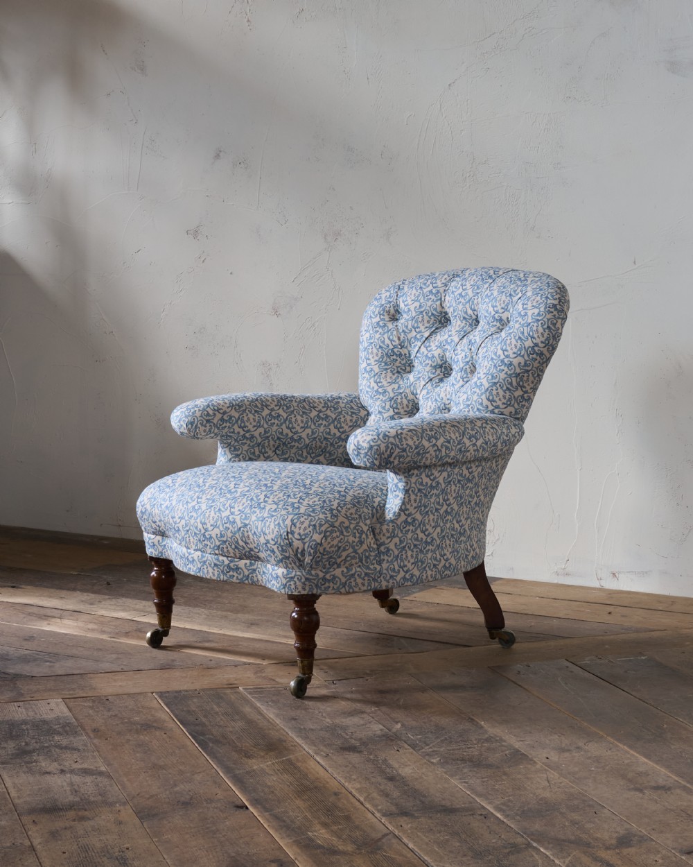 A Victorian Howard style armchair upholstered in blue and white scroll printed fabric with deep buttoning and turned mahogany legs on brass castors. View V