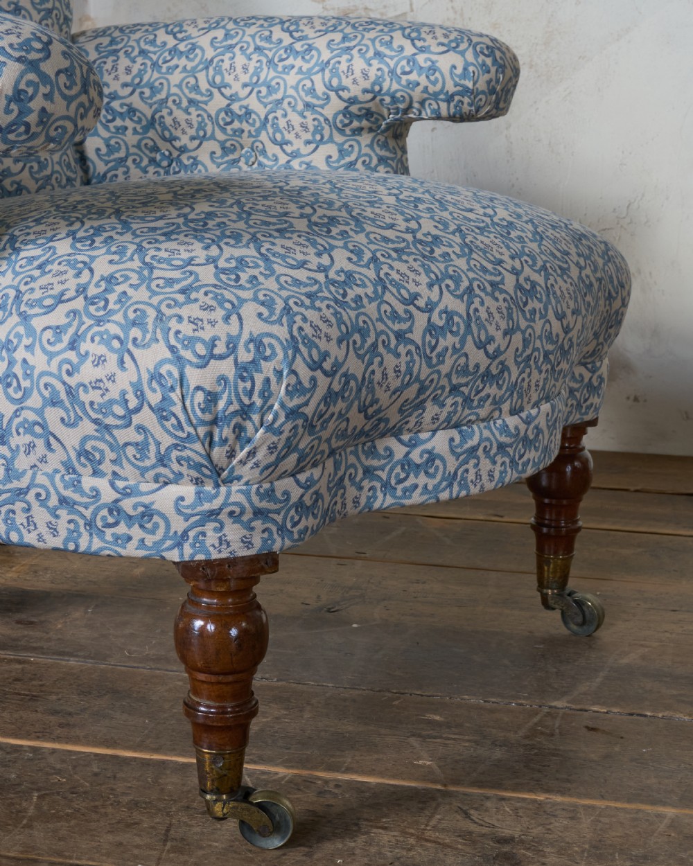 A Victorian Howard style armchair upholstered in blue and white scroll printed fabric with deep buttoning and turned mahogany legs on brass castors. View IX