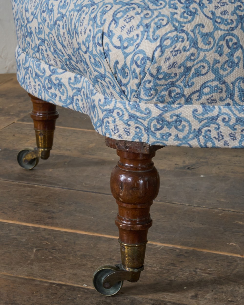 A Victorian Howard style armchair upholstered in blue and white scroll printed fabric with deep buttoning and turned mahogany legs on brass castors. View X