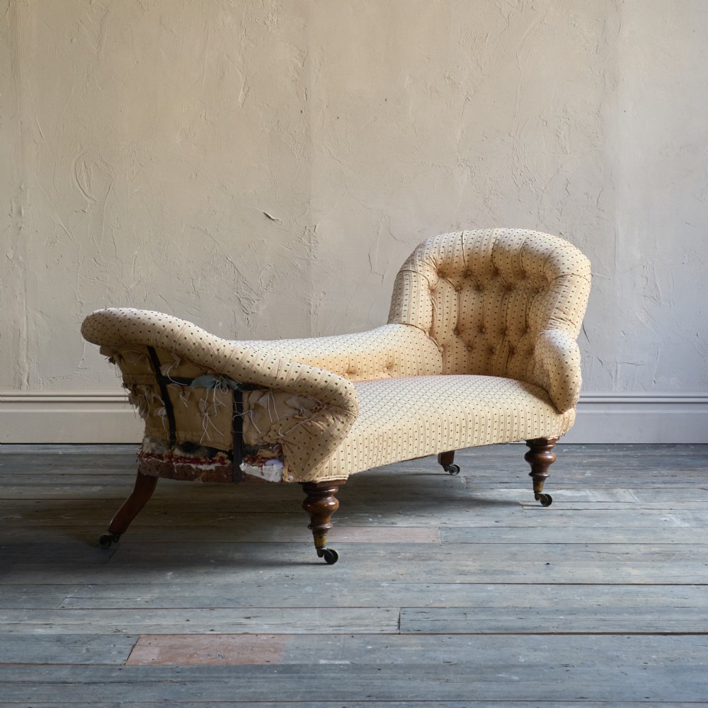 An antique Victorian chaise longue featuring a button-tufted spoon back, patterned upholstery, scrolled arm, and turned wooden legs with brass castors.