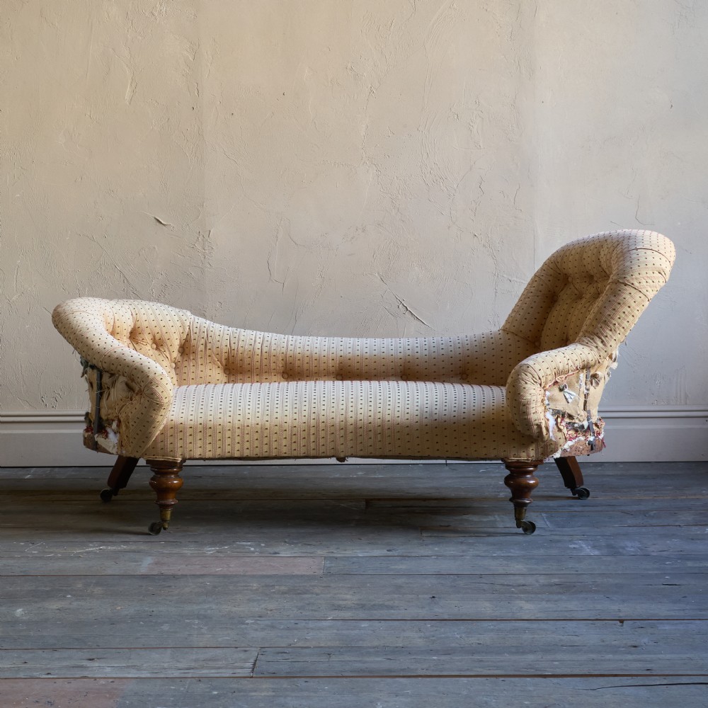 An antique Victorian chaise longue featuring a button-tufted spoon back, patterned upholstery, scrolled arm, and turned wooden legs with brass castors. View II
