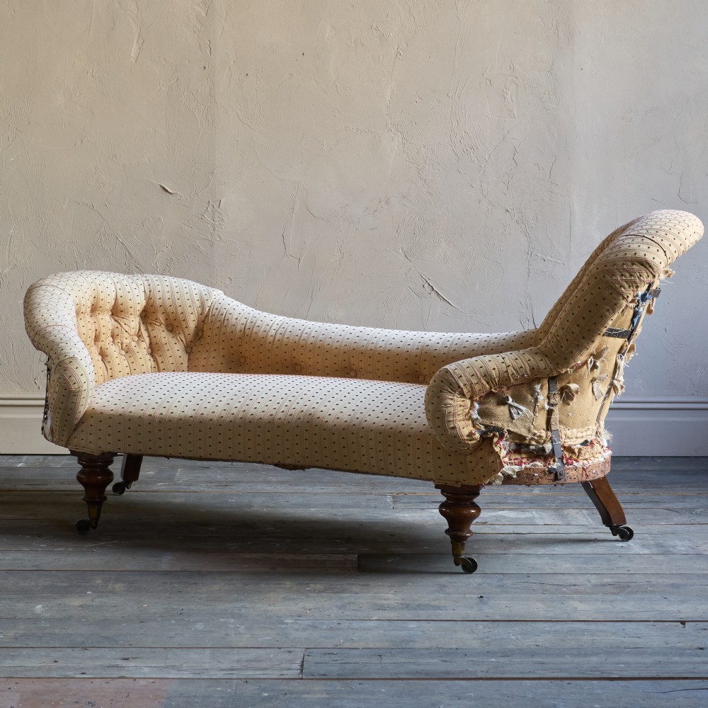 An antique Victorian chaise longue featuring a button-tufted spoon back, patterned upholstery, scrolled arm, and turned wooden legs with brass castors. View III