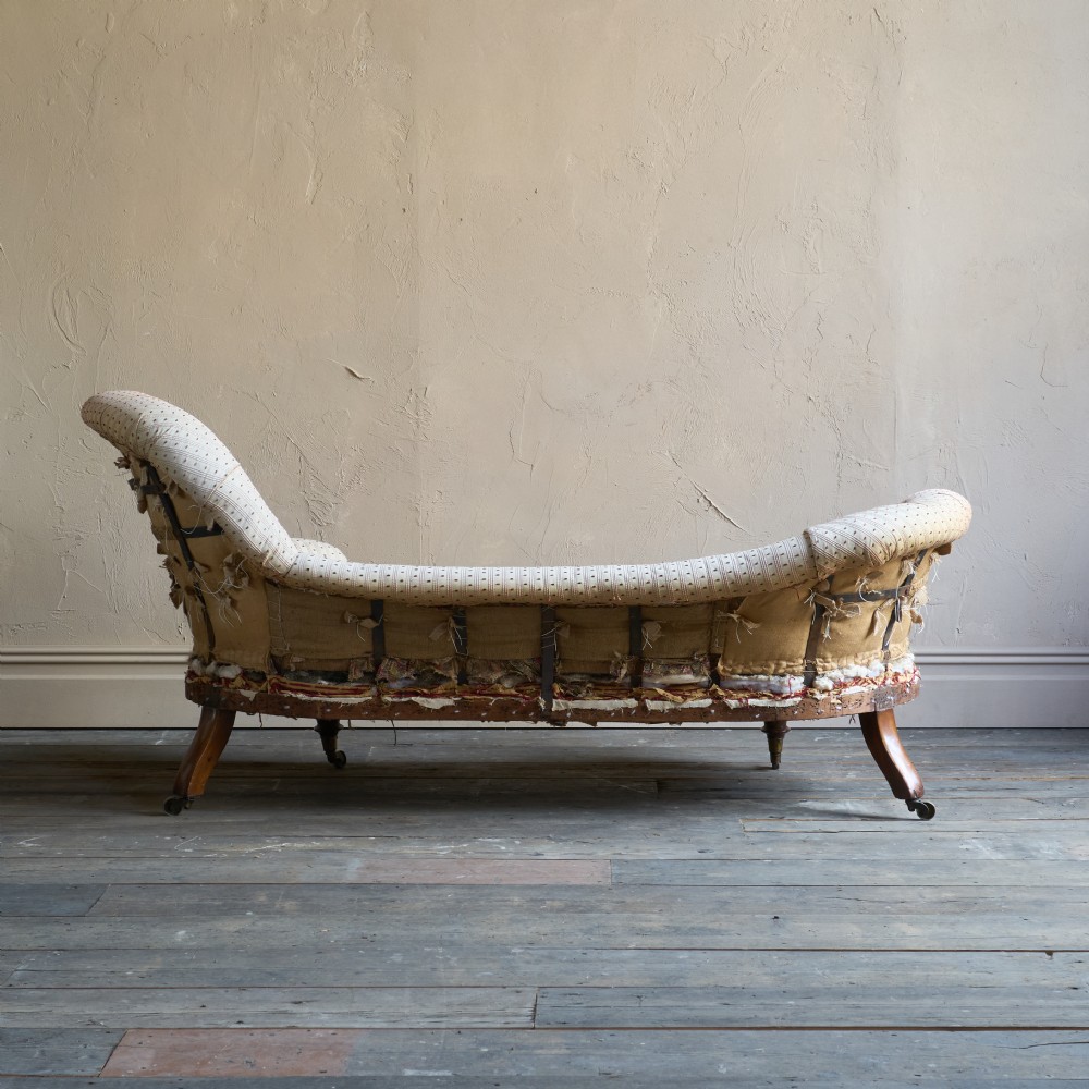 An antique Victorian chaise longue featuring a button-tufted spoon back, patterned upholstery, scrolled arm, and turned wooden legs with brass castors. View IV