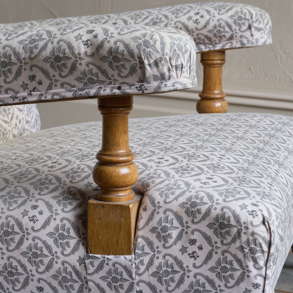 An antique open armchair featuring patterned grey ticking upholstery, a button-tufted backrest, padded armrests on turned wooden uprights, and short turned legs with brass castors. View III