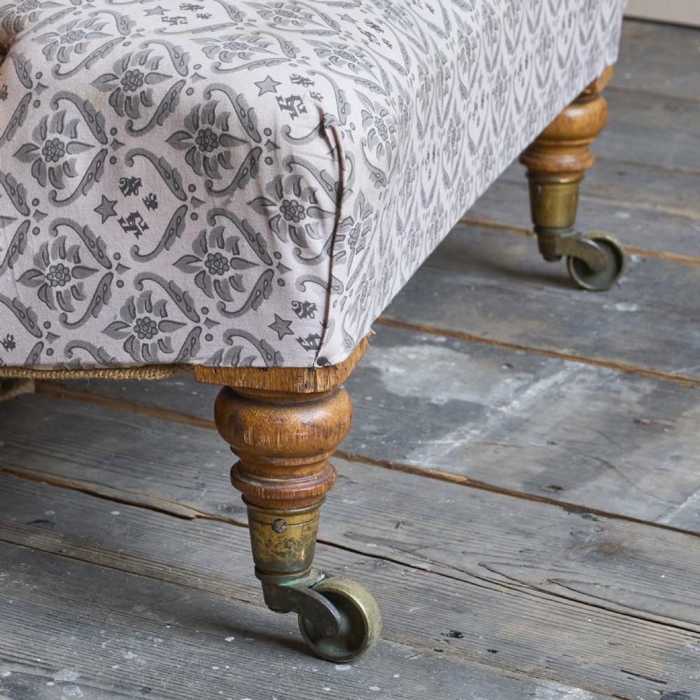 An antique open armchair featuring patterned grey ticking upholstery, a button-tufted backrest, padded armrests on turned wooden uprights, and short turned legs with brass castors. View IV