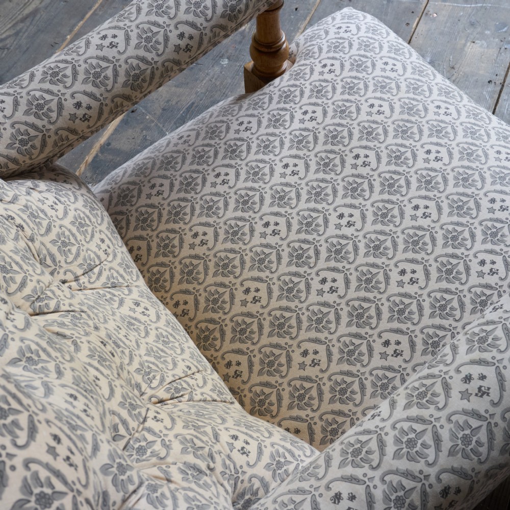 An antique open armchair featuring patterned grey ticking upholstery, a button-tufted backrest, padded armrests on turned wooden uprights, and short turned legs with brass castors. View VI