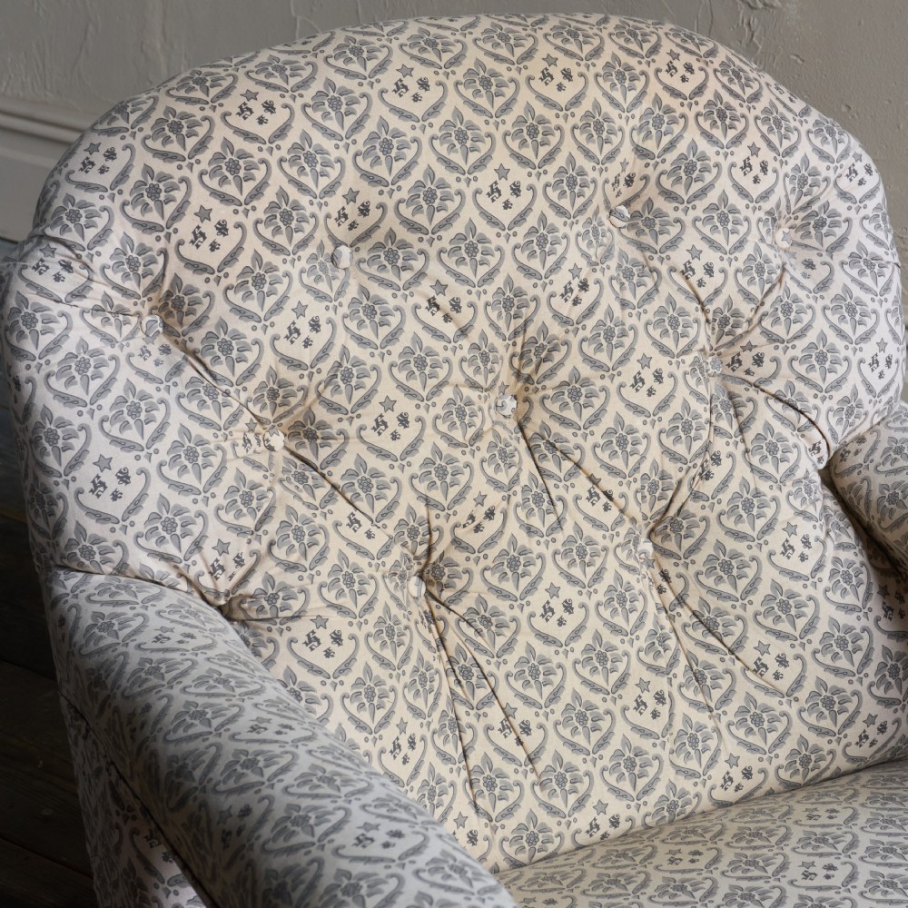 An antique open armchair featuring patterned grey ticking upholstery, a button-tufted backrest, padded armrests on turned wooden uprights, and short turned legs with brass castors. View VII