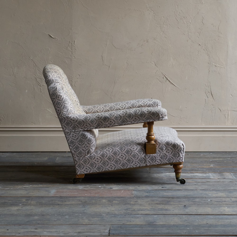 An antique open armchair featuring patterned grey ticking upholstery, a button-tufted backrest, padded armrests on turned wooden uprights, and short turned legs with brass castors. View VIII