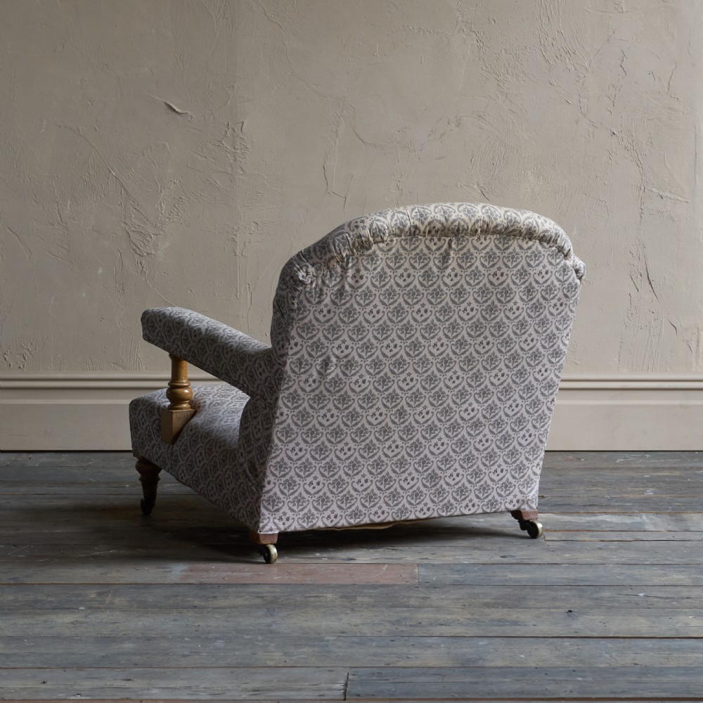An antique open armchair featuring patterned grey ticking upholstery, a button-tufted backrest, padded armrests on turned wooden uprights, and short turned legs with brass castors. View IX