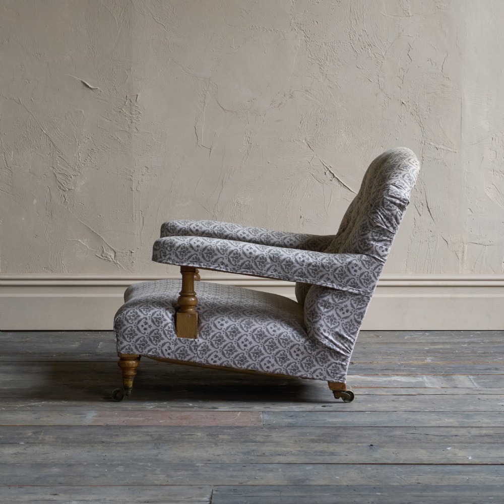 An antique open armchair featuring patterned grey ticking upholstery, a button-tufted backrest, padded armrests on turned wooden uprights, and short turned legs with brass castors. View X