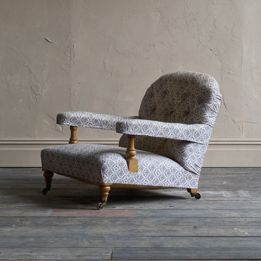 An antique open armchair featuring patterned grey ticking upholstery, a button-tufted backrest, padded armrests on turned wooden uprights, and short turned legs with brass castors. View XI