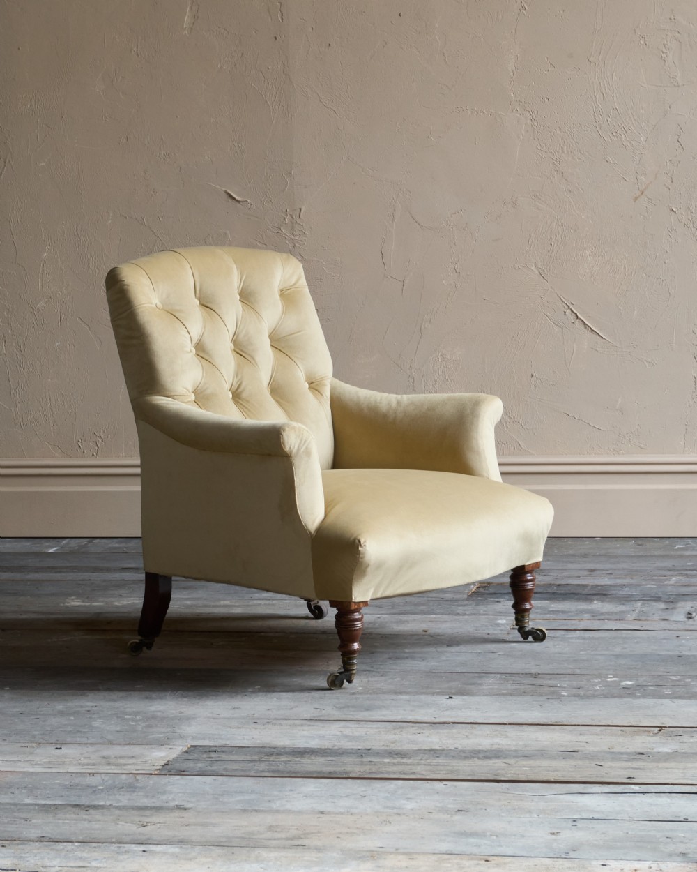 A deep-seated Victorian armchair upholstered in gold velvet with a button-backed backrest, turned mahogany front legs, and brass castors.