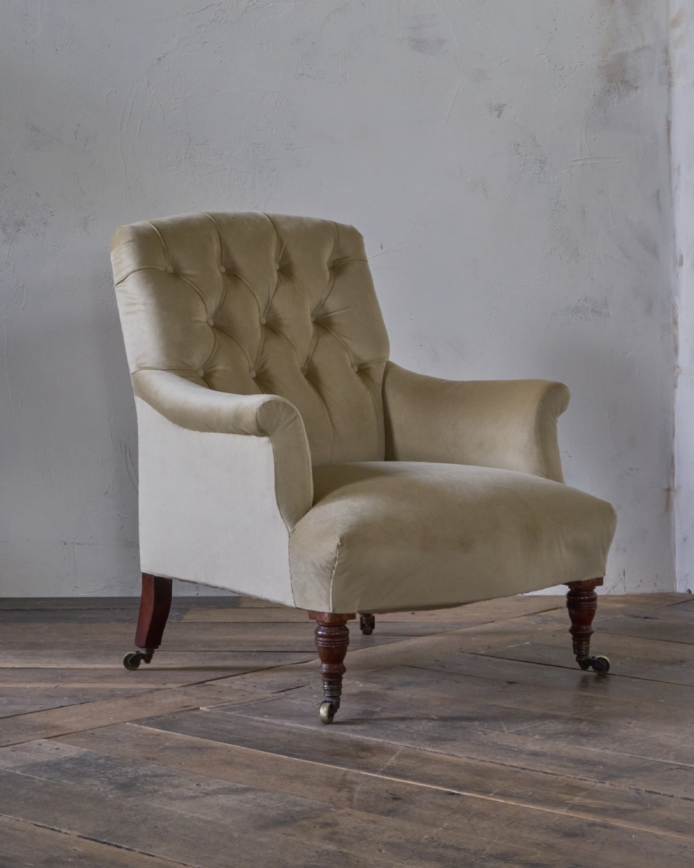 A deep-seated Victorian armchair upholstered in gold velvet with a button-backed backrest, turned mahogany front legs, and brass castors. View V