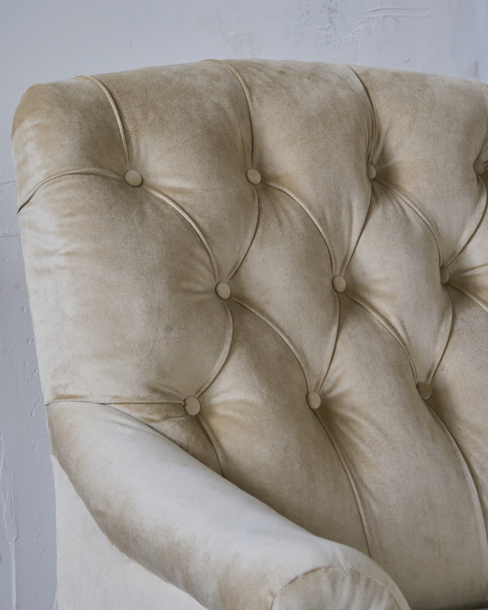 A deep-seated Victorian armchair upholstered in gold velvet with a button-backed backrest, turned mahogany front legs, and brass castors. View VI