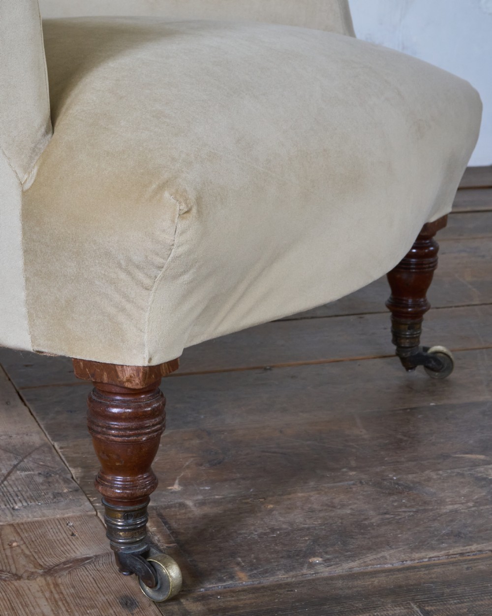A deep-seated Victorian armchair upholstered in gold velvet with a button-backed backrest, turned mahogany front legs, and brass castors. View VII