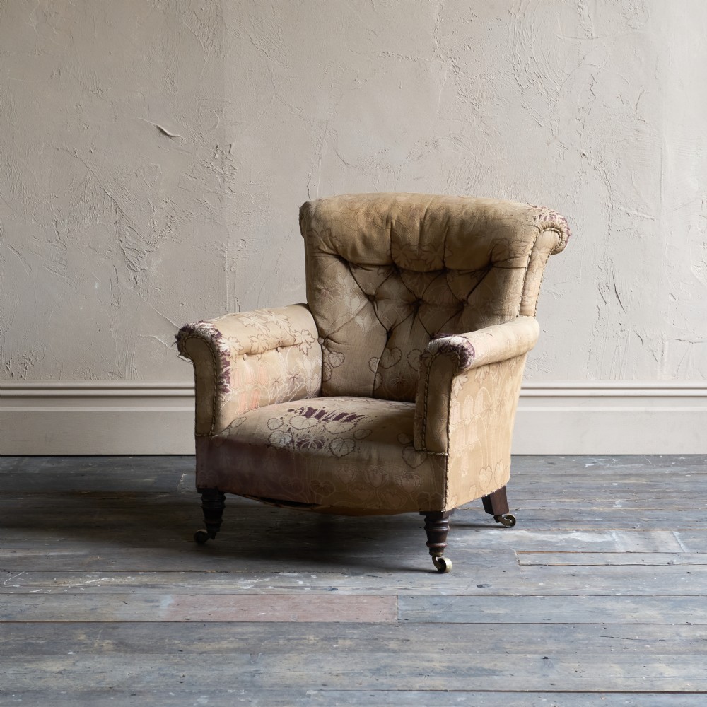 A low-seated Victorian style upholstered easy chair featuring a deep-buttoned backrest, rolled arms, floral damask pattern, and turned timber front legs with brass castors.
