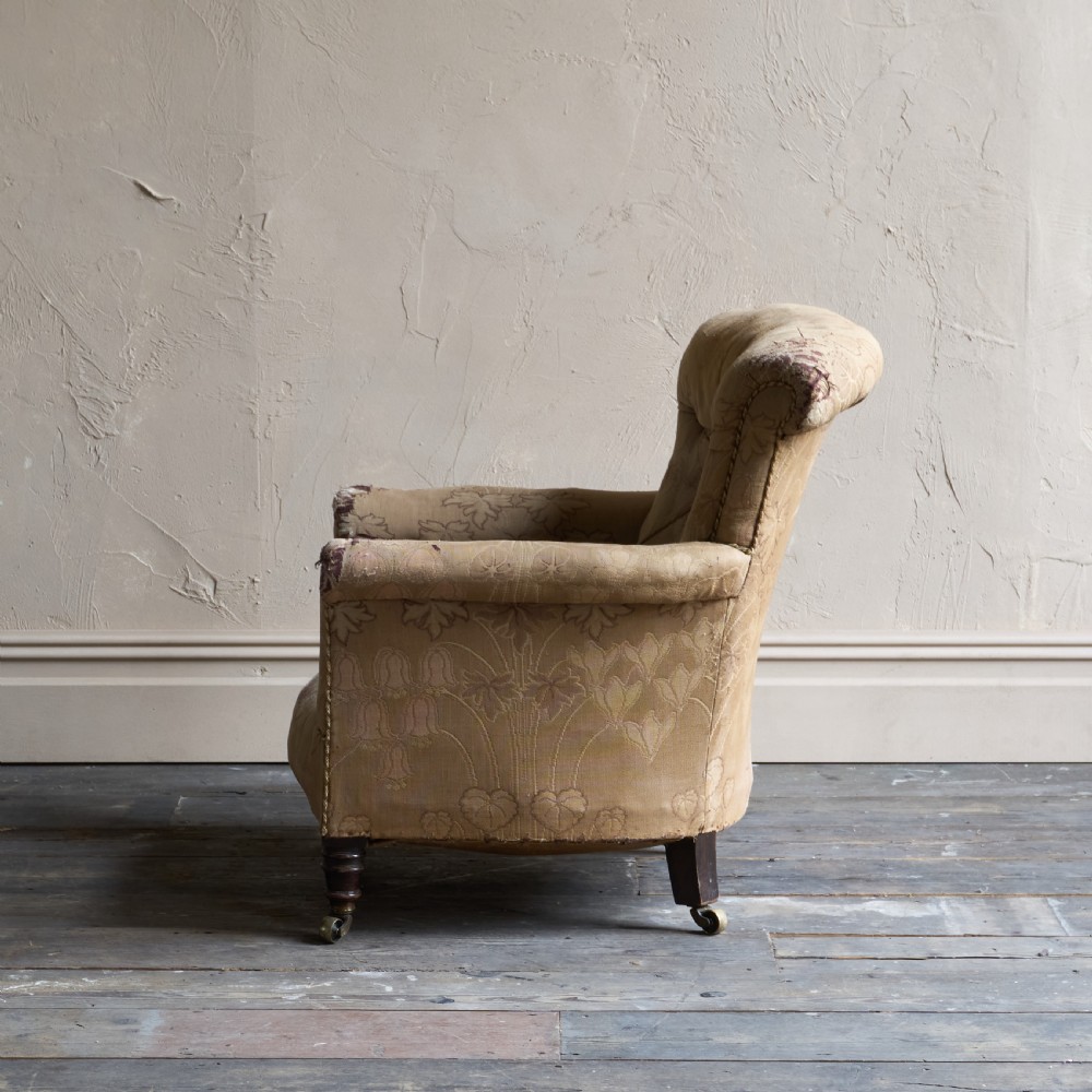 A low-seated Victorian style upholstered easy chair featuring a deep-buttoned backrest, rolled arms, floral damask pattern, and turned timber front legs with brass castors. View IV