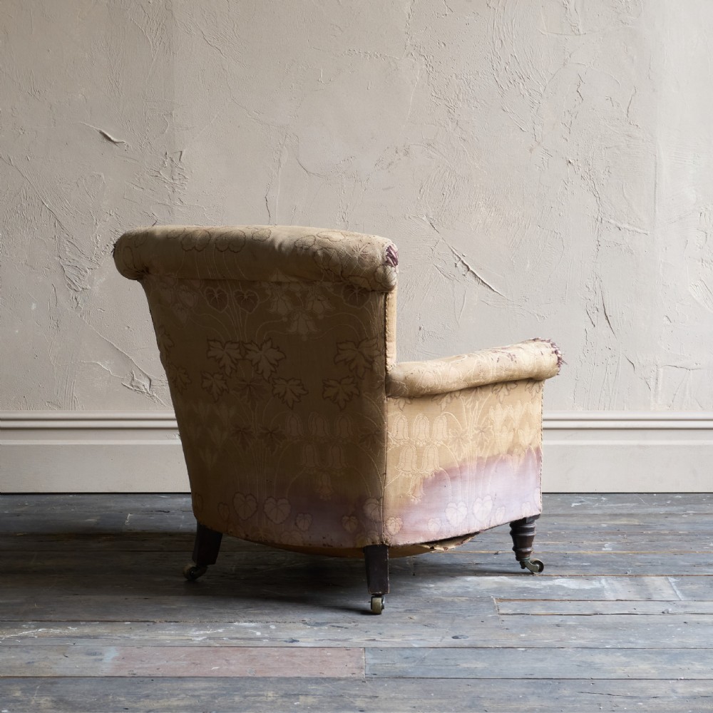 A low-seated Victorian style upholstered easy chair featuring a deep-buttoned backrest, rolled arms, floral damask pattern, and turned timber front legs with brass castors. View V