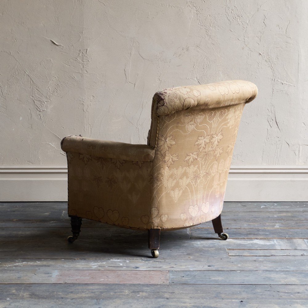 A low-seated Victorian style upholstered easy chair featuring a deep-buttoned backrest, rolled arms, floral damask pattern, and turned timber front legs with brass castors. View VI