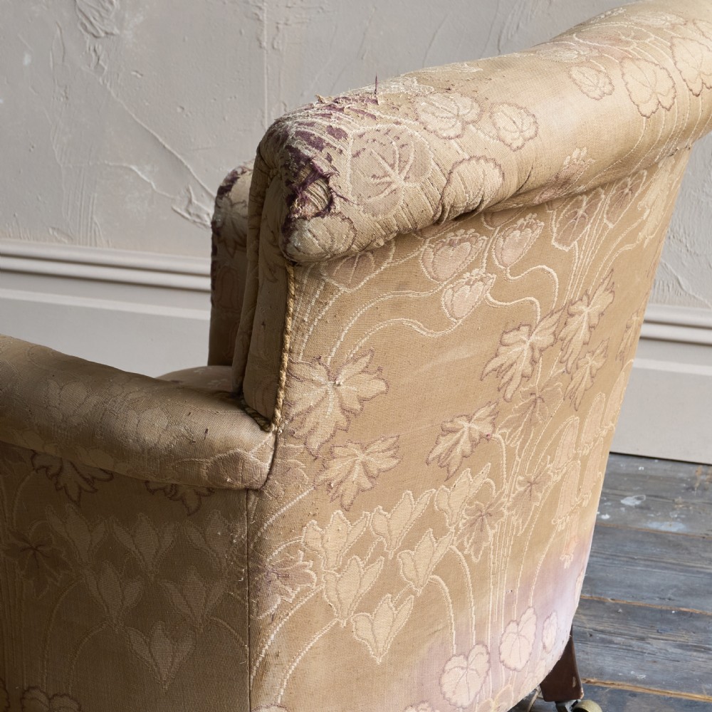 A low-seated Victorian style upholstered easy chair featuring a deep-buttoned backrest, rolled arms, floral damask pattern, and turned timber front legs with brass castors. View VII