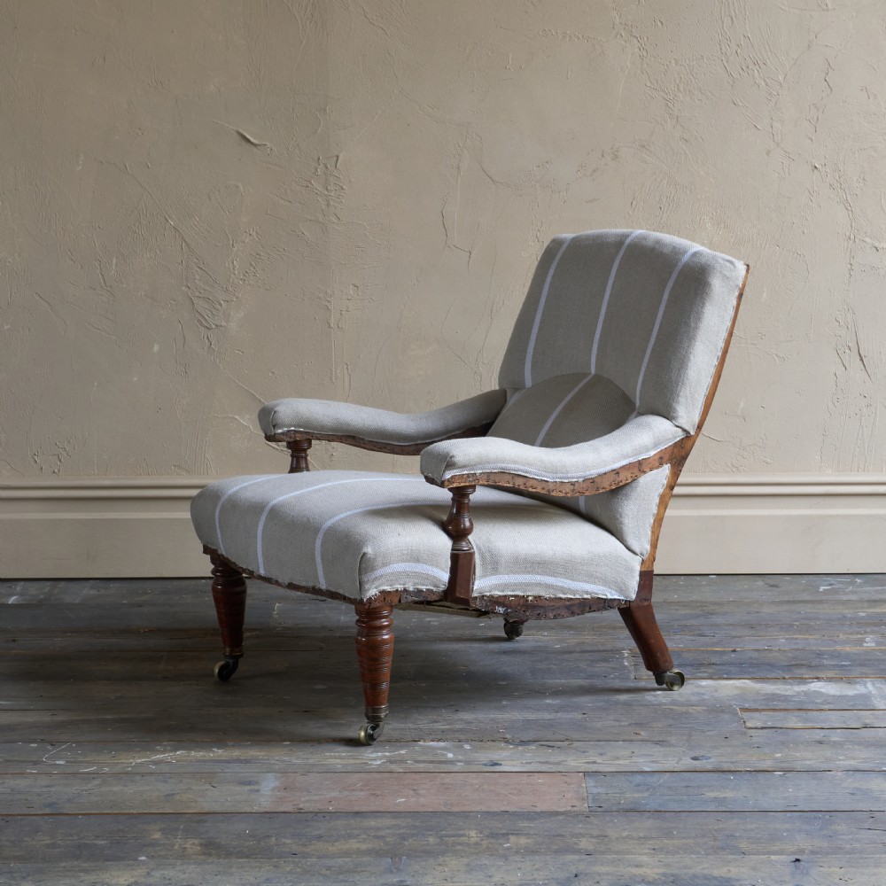 An antique open armchair upholstered in cream fabric with vertical white ticking stripes, featuring turned wooden front legs with brass castors. View III