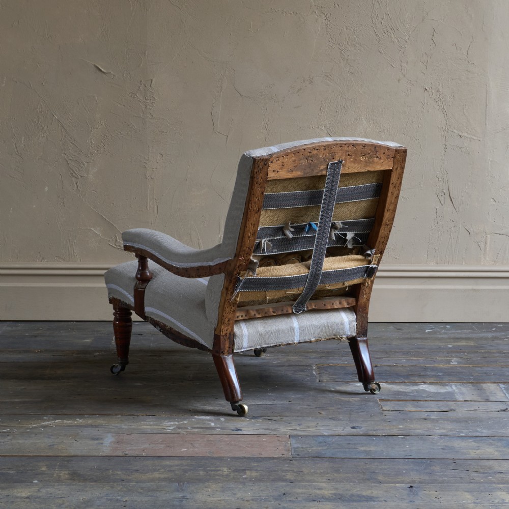 An antique open armchair upholstered in cream fabric with vertical white ticking stripes, featuring turned wooden front legs with brass castors. View IV