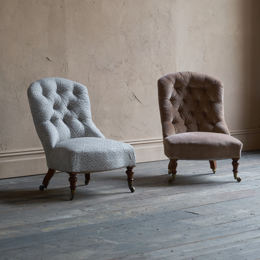 A pair of Victorian low-slung button-backed slipper chairs with turned wooden legs on brass castors, one in taupe velvet and one in patterned blue and white fabric. View IX