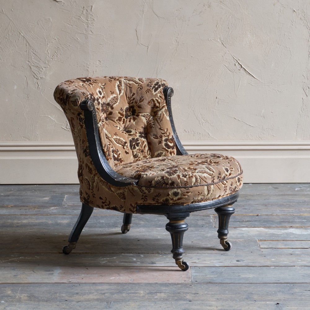 A Victorian low-seated tub chair upholstered in brown patterned floral velvet with ebonised turned legs, gilt accents, and brass castors.