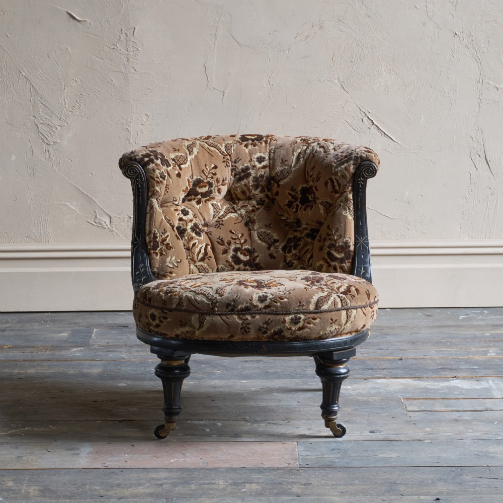 A Victorian low-seated tub chair upholstered in brown patterned floral velvet with ebonised turned legs, gilt accents, and brass castors. View II