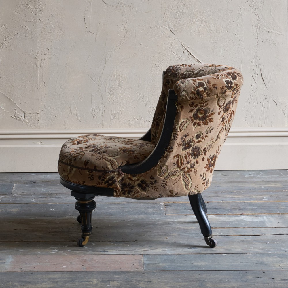 A Victorian low-seated tub chair upholstered in brown patterned floral velvet with ebonised turned legs, gilt accents, and brass castors. View IV